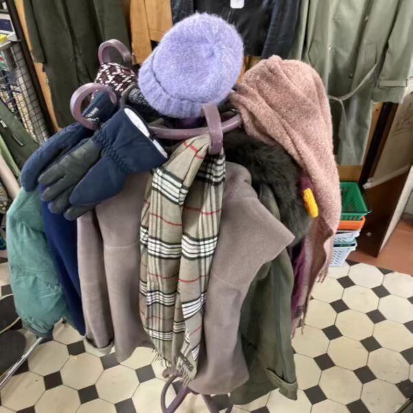 Kleiderständer mit Wintersachen aus dem Brocki Ein flacher geflochtener Korb voller bunter Hühner-Glaseier, dahinter in weissen Lettern der Schriftzug "Ostern" auf dem Ostertisch im Brocki, alles Material aus Haus- und Wohnungsräumungen